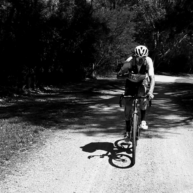 Skingrowsback Transcend Racing Series transition 1.5 litre hydration backpack black and white male cyclist taking a sip from the hose on a gravel road animated gif