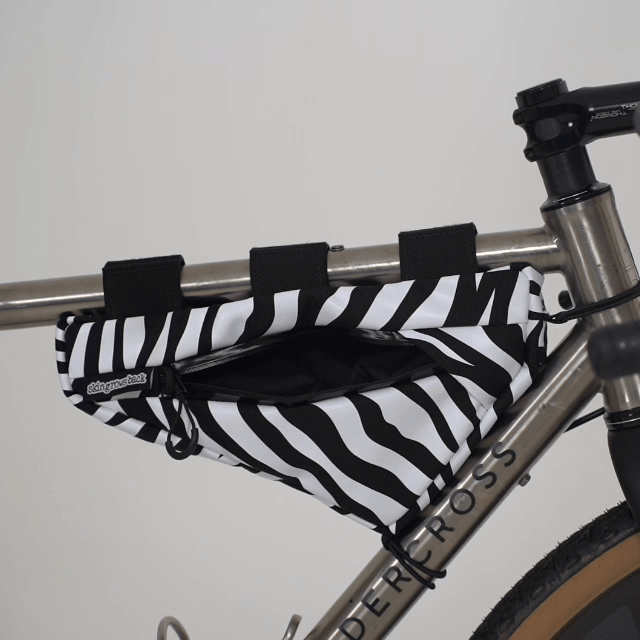 skingrowsback wedge frame bag zebra gif hand putting items inside a frame bag on a titanium bike with a white background