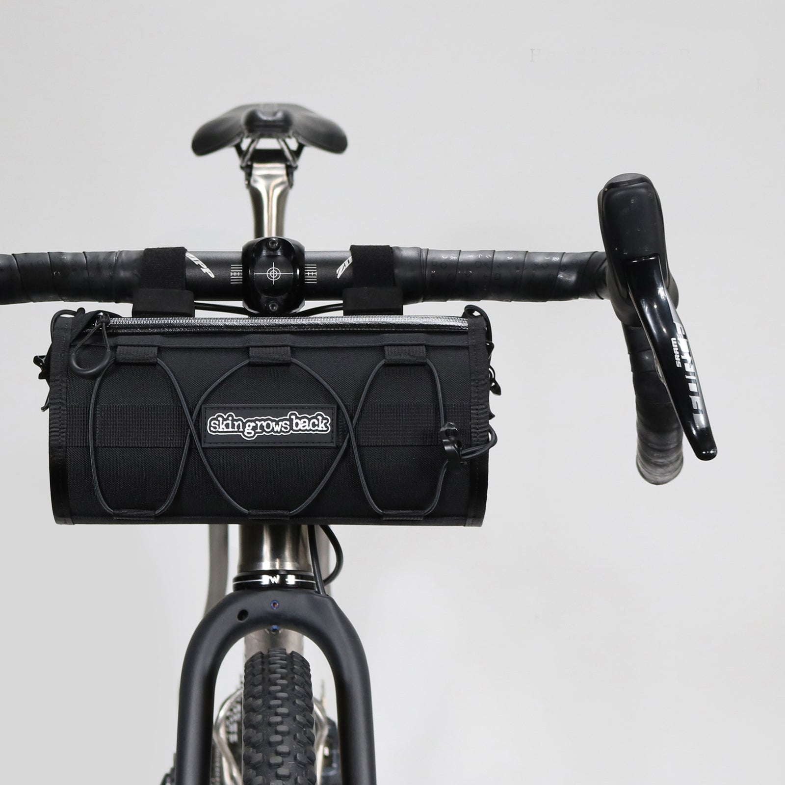 skingrowsback lunchbox handlebar bag black mounted to a gravel bike against a grey background