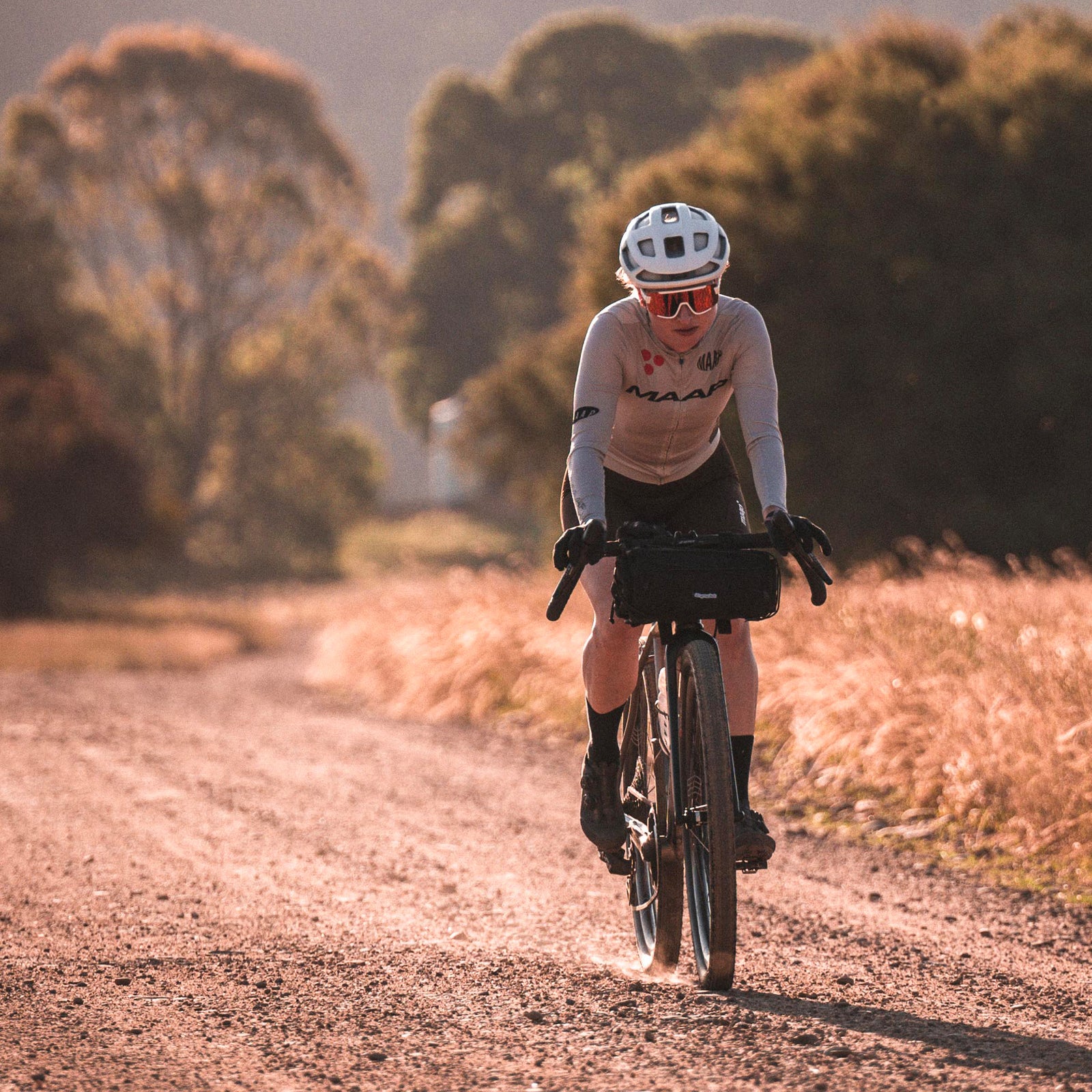 Skingrowsback overnighter handlebar bag black attached to the handlebars - woman cycling on a dirt road with a scenic background