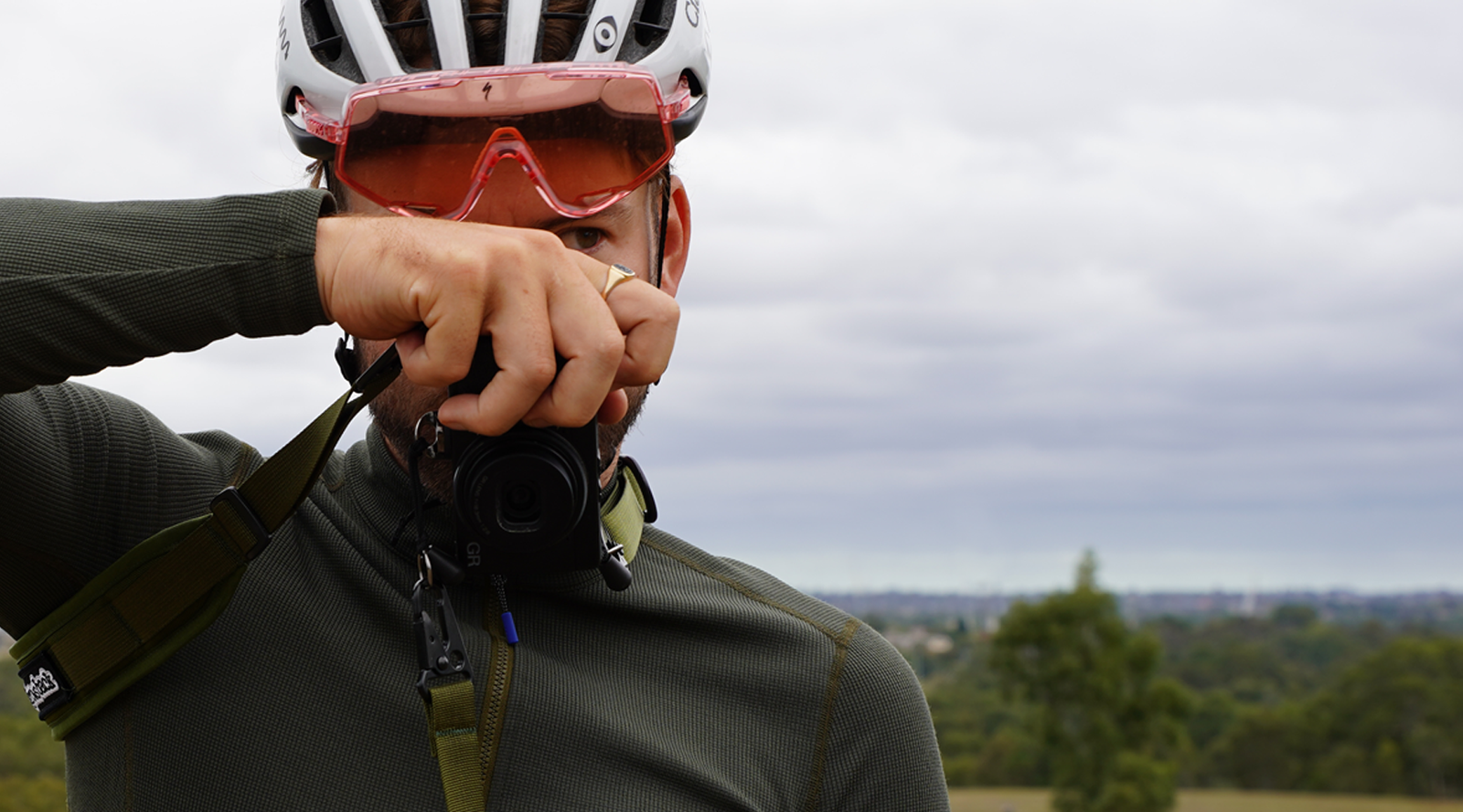 Skingrowsback 3Point Cycling Camera Strap — young male cyclist capturing a shot with a camera on the bike