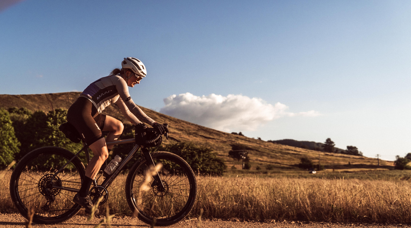 Skingrowsback overnighter handlebar bag black attached to the handlebars - woman cycling on a dirt road with a scenic background