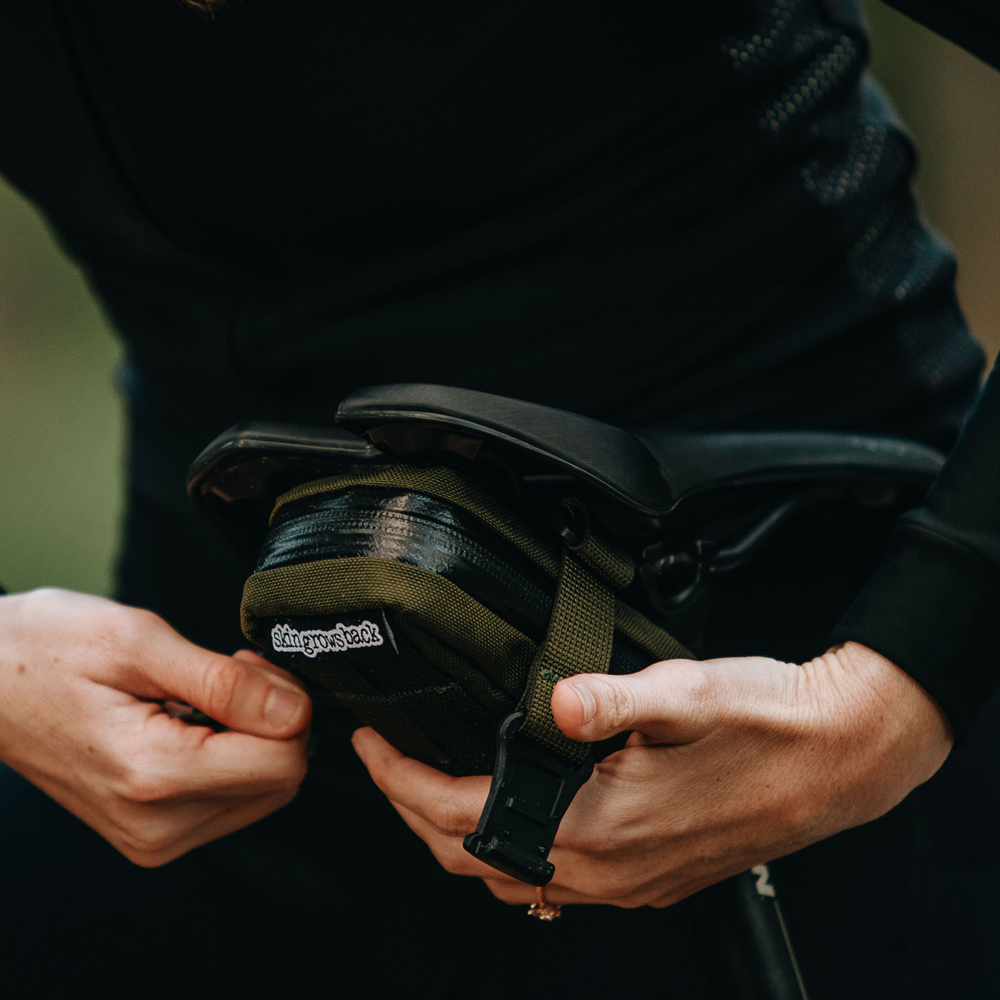 Skingrowsback Plan B Saddle Bag in olive — woman in black attaching it to her bike saddle