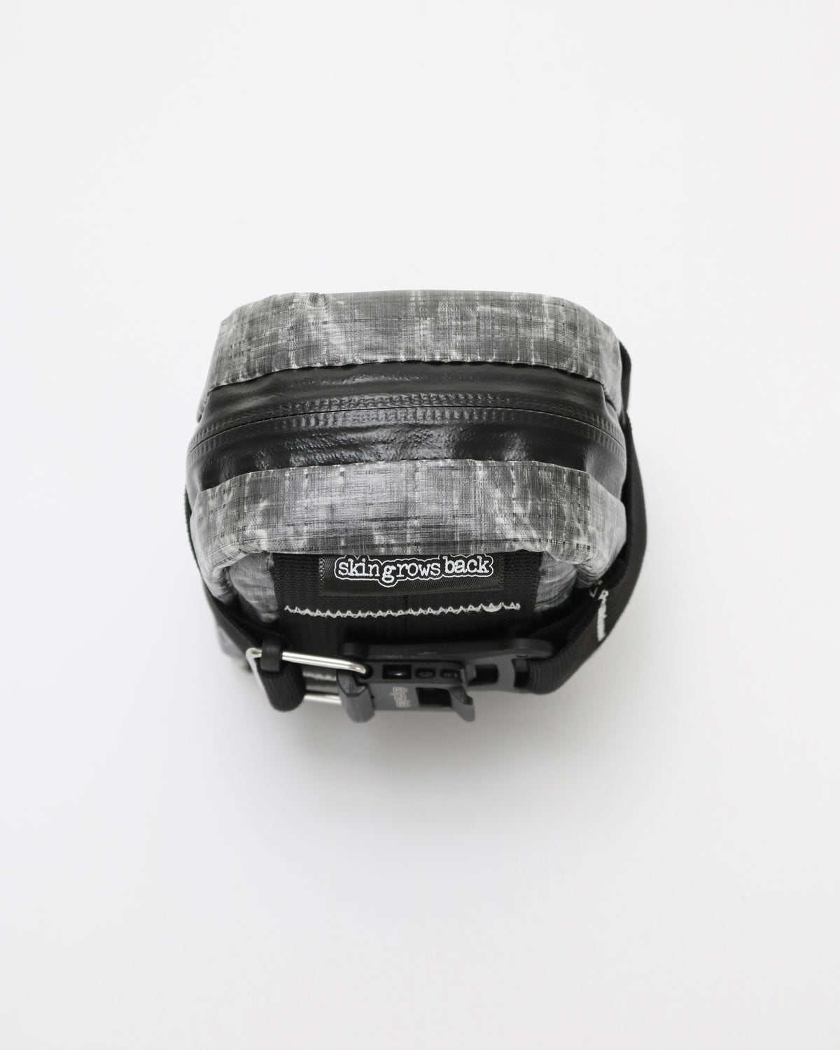 A small rectangular zippered pouch with a black and white marbled or textured pattern, featuring a black zipper, black side straps, and a black label that reads 'skingrowsback'.