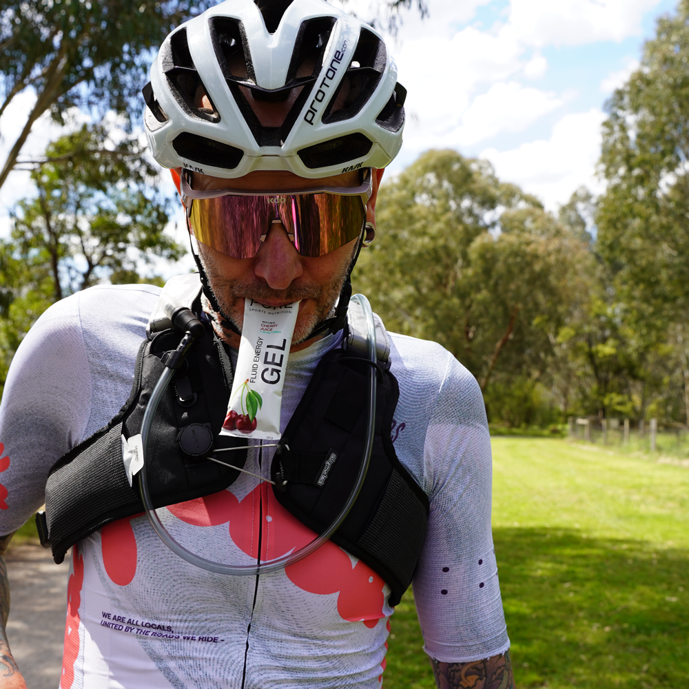 Skingrowsback Transcend Racing Series 1.5 Litre Hydration Backpack — male cyclist riding on Australian gravel road taking a gel